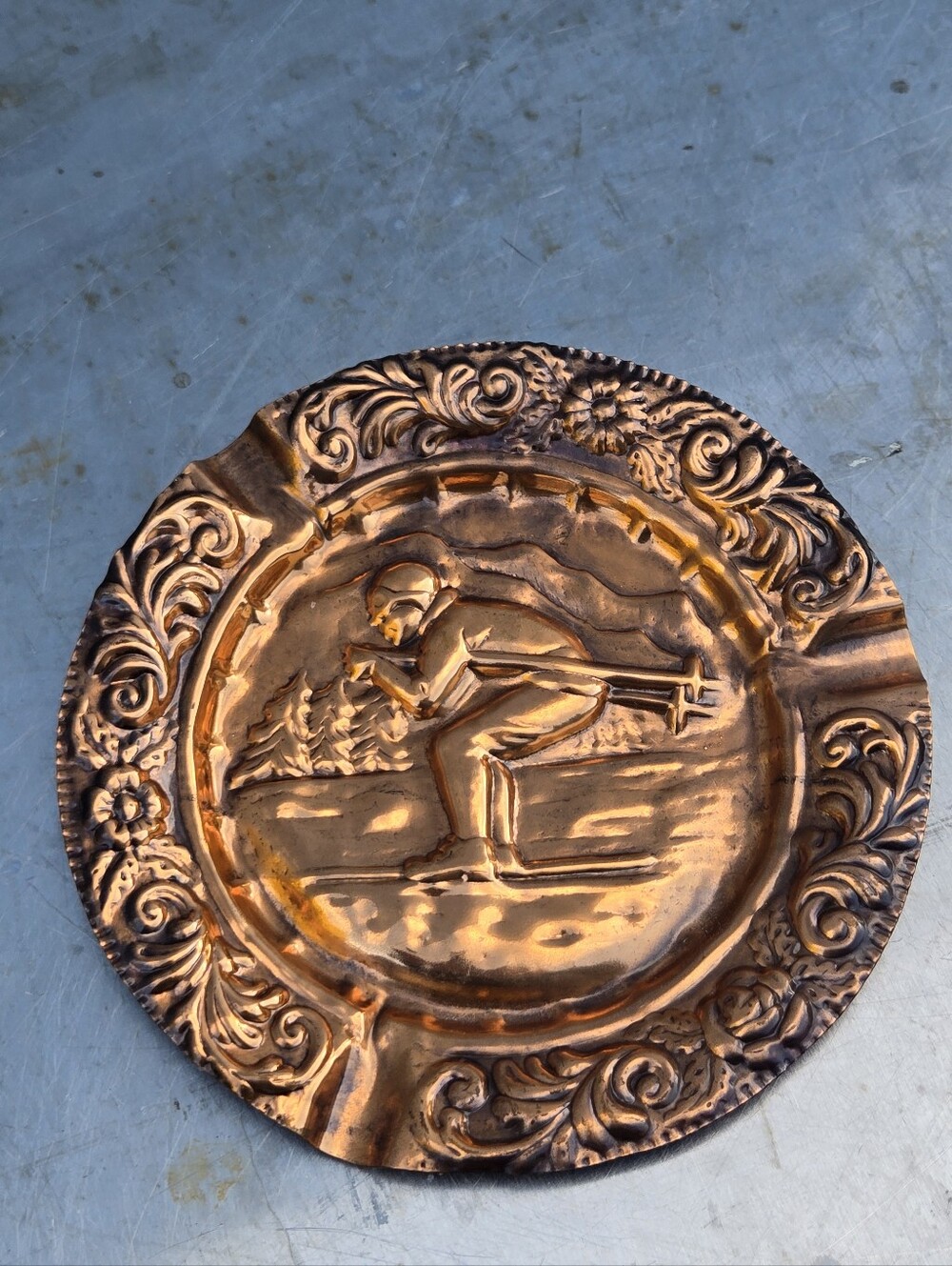 Vintage copper ashtray with a central embossed skier motif.